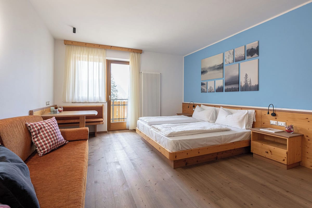 A bedroom with a wooden bed, a wooden nightstand, a wooden bench, and a view of the outdoors through a window.