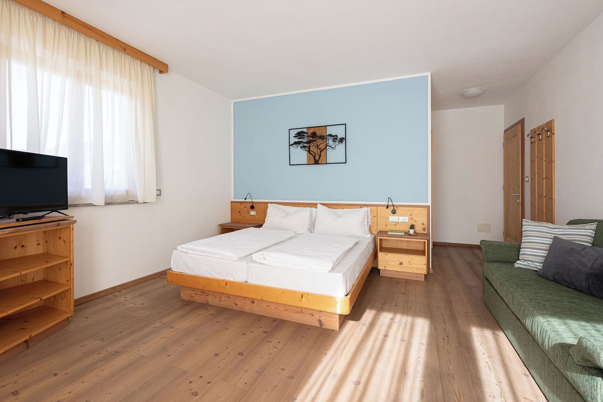 A bedroom with a wooden bed, a television on a wooden stand, a green sofa, and a painting on the wall.