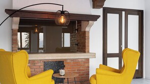 A brick fireplace with a hanging light fixture, two yellow chairs, and a small table. - Grünwald (Salorno)