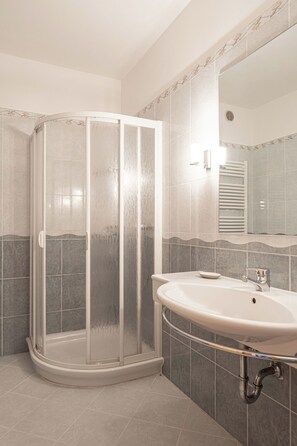 A bathroom with a glass-enclosed shower, a sink, and a mirror. - Grünwald (Salorno)
