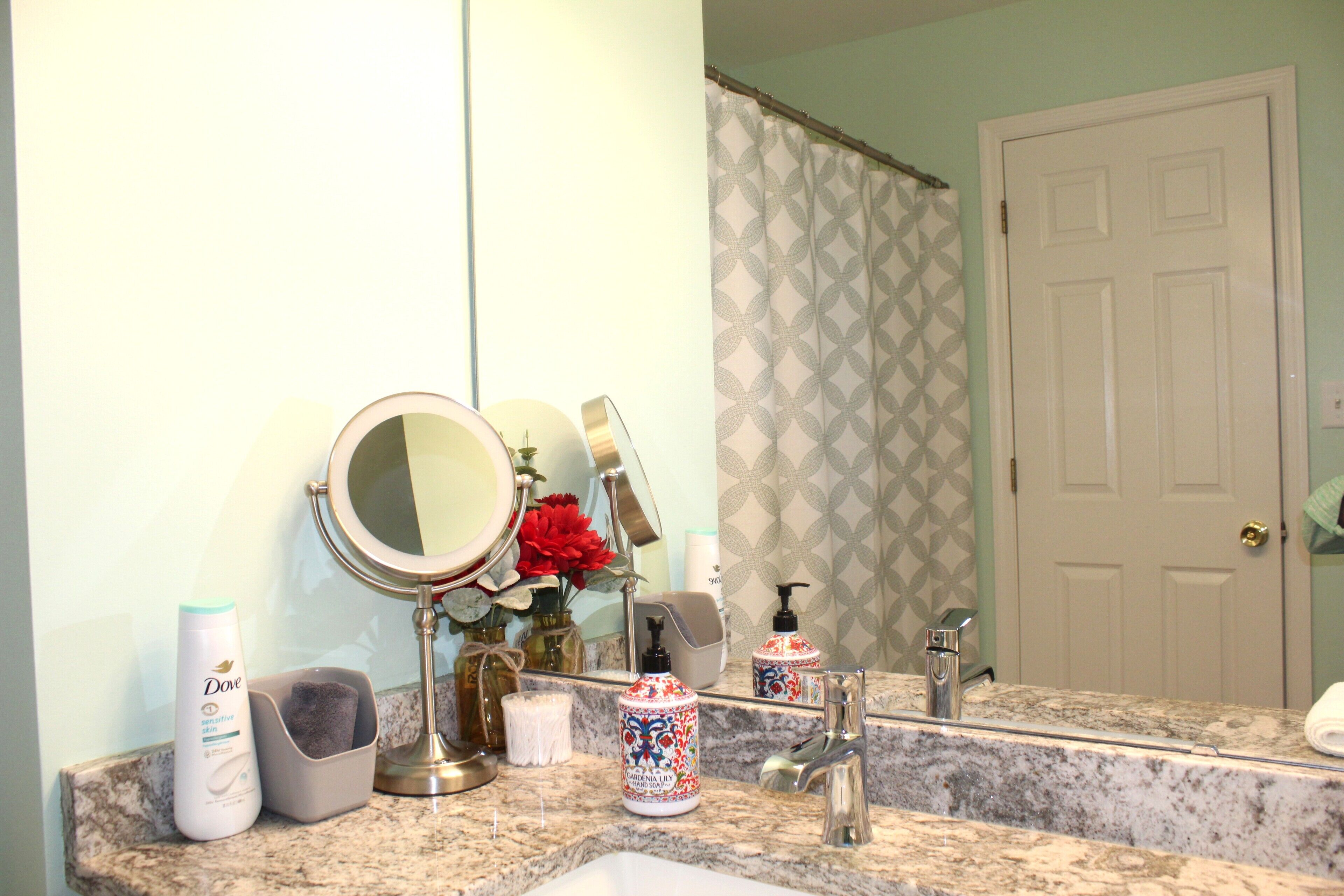 A bathroom with a granite countertop, a sink, a mirror, a shower curtain, and toiletries.