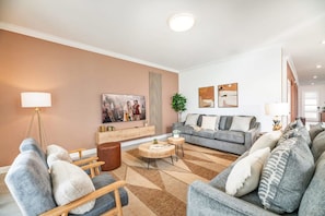 Een moderne woonkamer met een bank, fauteuils, een salontafel en een schilderij aan de muur.