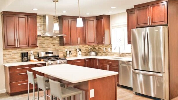 A modern kitchen with wooden cabinets, a stainless steel refrigerator, and a central island with bar stools. - Charming, Brand New Home in Greenlake, 4br3ba (Seattle)