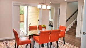 A dining area with a glass table and orange chairs, a staircase, and a sliding glass door leading to a backyard. - Charming, Brand New Home in Greenlake, 4br3ba (Seattle)