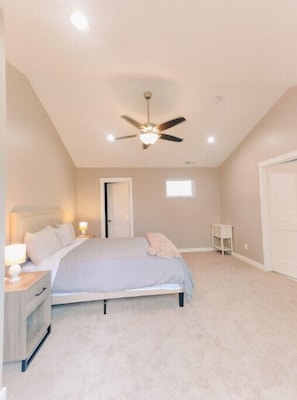 A bedroom with a bed, bedside table, nightstand, ceiling fan, and a small window.