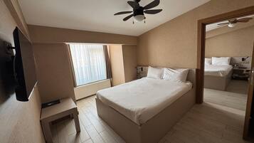 A hotel room with a bed, a ceiling fan, a window with curtains, a bedside table, and a mirror.