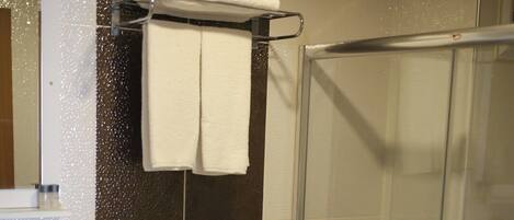 Un baño con inodoro, cabina de ducha de vidrio y toallero con toallas dobladas.