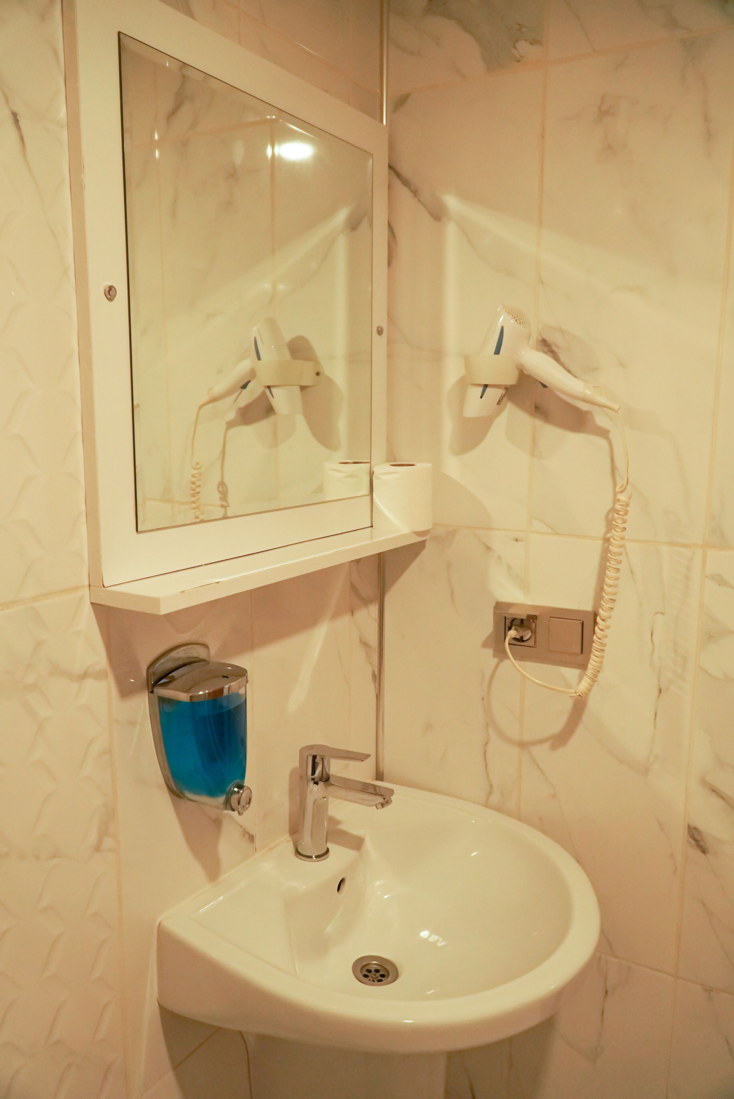 Un baño con un lavamanos blanco, un espejo y un secador de pelo montado en la pared.