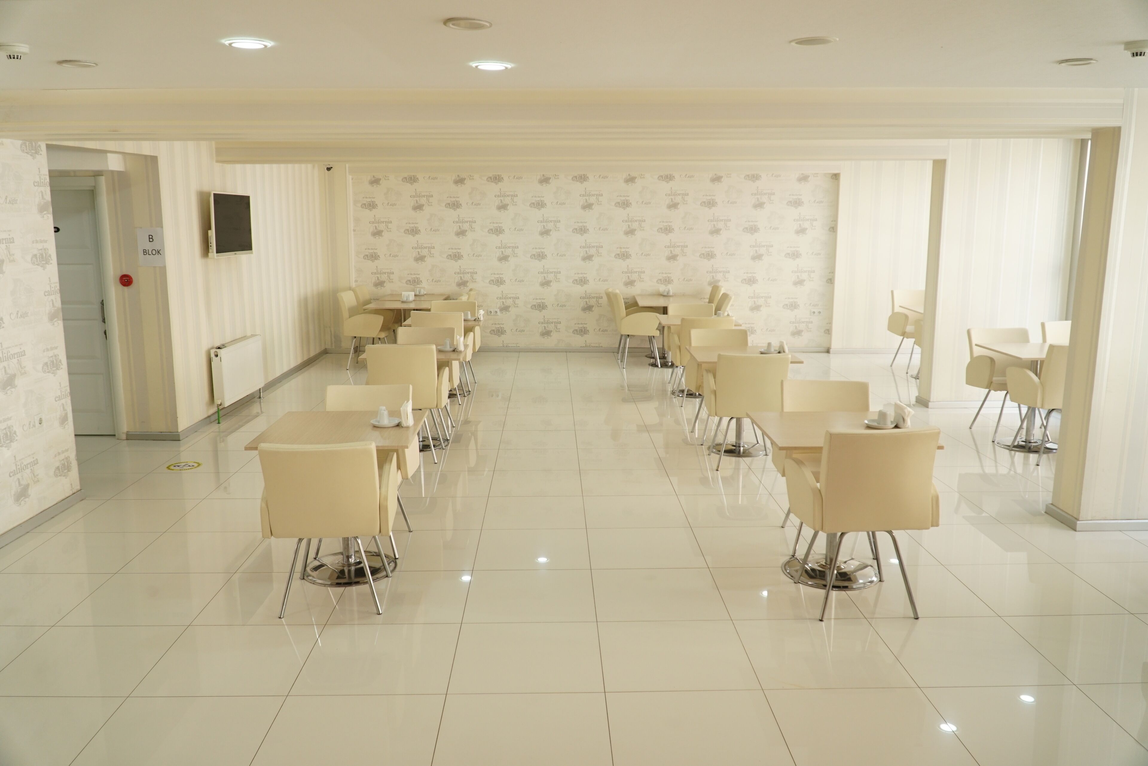 A spacious, well-lit conference room with a long table and multiple chairs, white walls with subtle patterns, and a tiled floor.