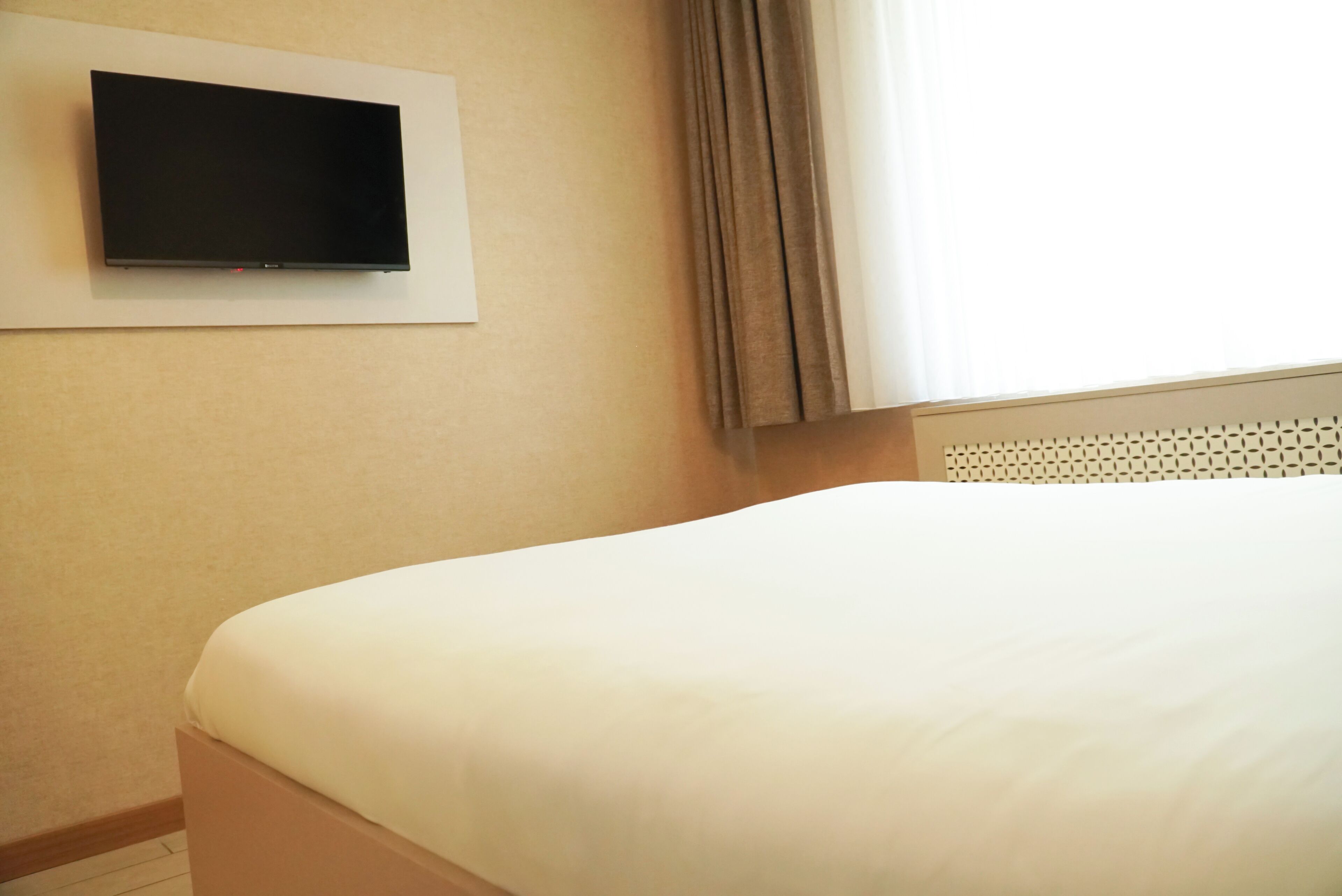 Una habitación de hotel con cama, televisión montada en la pared y ventana con cortinas.