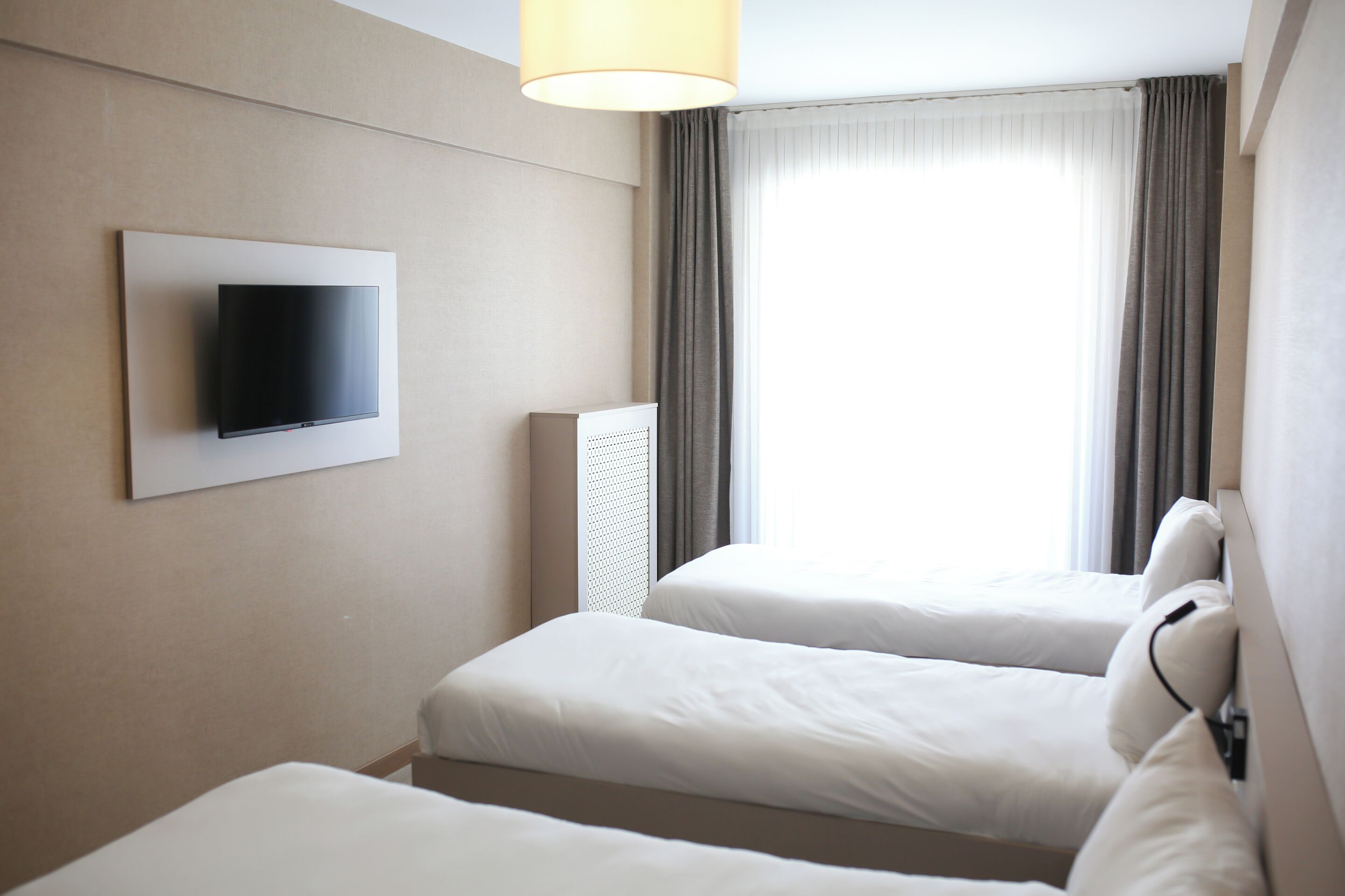 A hotel room with two beds, a flat-screen TV mounted on the wall, and a large window with curtains.