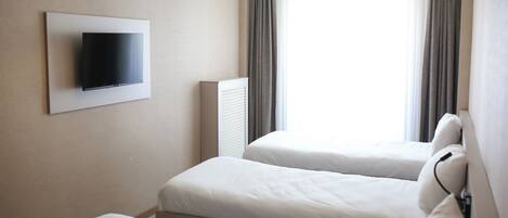 Habitación de hotel con dos camas, un televisor de pantalla plana montado en la pared y un ventanal con cortinas.