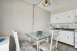A compact kitchen with white cabinets, a glass-top table, and patterned chairs. - Beachfront Fourth-Floor Condo w/ Community Pool! (North Wildwood)