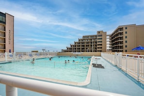 A swimming pool with people swimming, surrounded by buildings with balconies. - Beachfront Fourth-Floor Condo w/ Community Pool! (North Wildwood)
