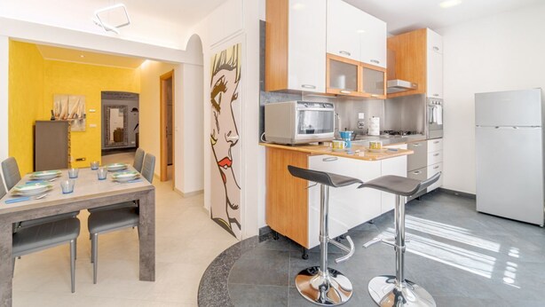 Una cocina moderna con armarios blancos y de madera, un refrigerador de acero inoxidable y un comedor con mesa y sillas.