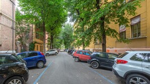 Una calle bordeada de coches aparcados y árboles, con edificios a ambos lados y un cielo despejado.