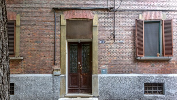 Un edificio de ladrillo con puerta de madera, una ventana con contraventanas y el número '50' en la pared.