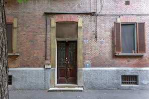 Um edifício de tijolos com uma porta de madeira, uma janela com portaria e o número '50' na parede.