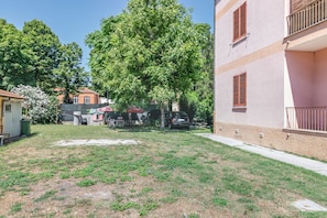 A residential area with a grassy yard, a large tree, and a building with balconies.