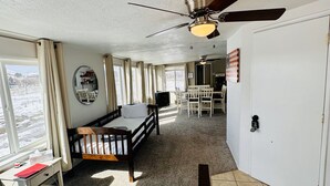 Quarto de hotel com cama, escrivaninha, cadeira, ventoinha no teto e vista para o exterior.