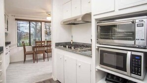 Uma cozinha moderna com armários brancos, fogão a gás e duas micro-ondas embutidas.