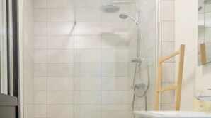 Une salle de bain moderne avec une douche, un petit tabouret en bois et un lavabo blanc avec un miroir.