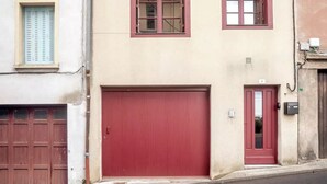 Un bâtiment avec une porte de garage rouge, une façade beige et une petite fenêtre avec des volets.