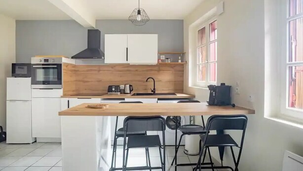 Une cuisine moderne avec un îlot central, des tabourets de bar noirs et une fenêtre agrémentée de rideaux roses.
