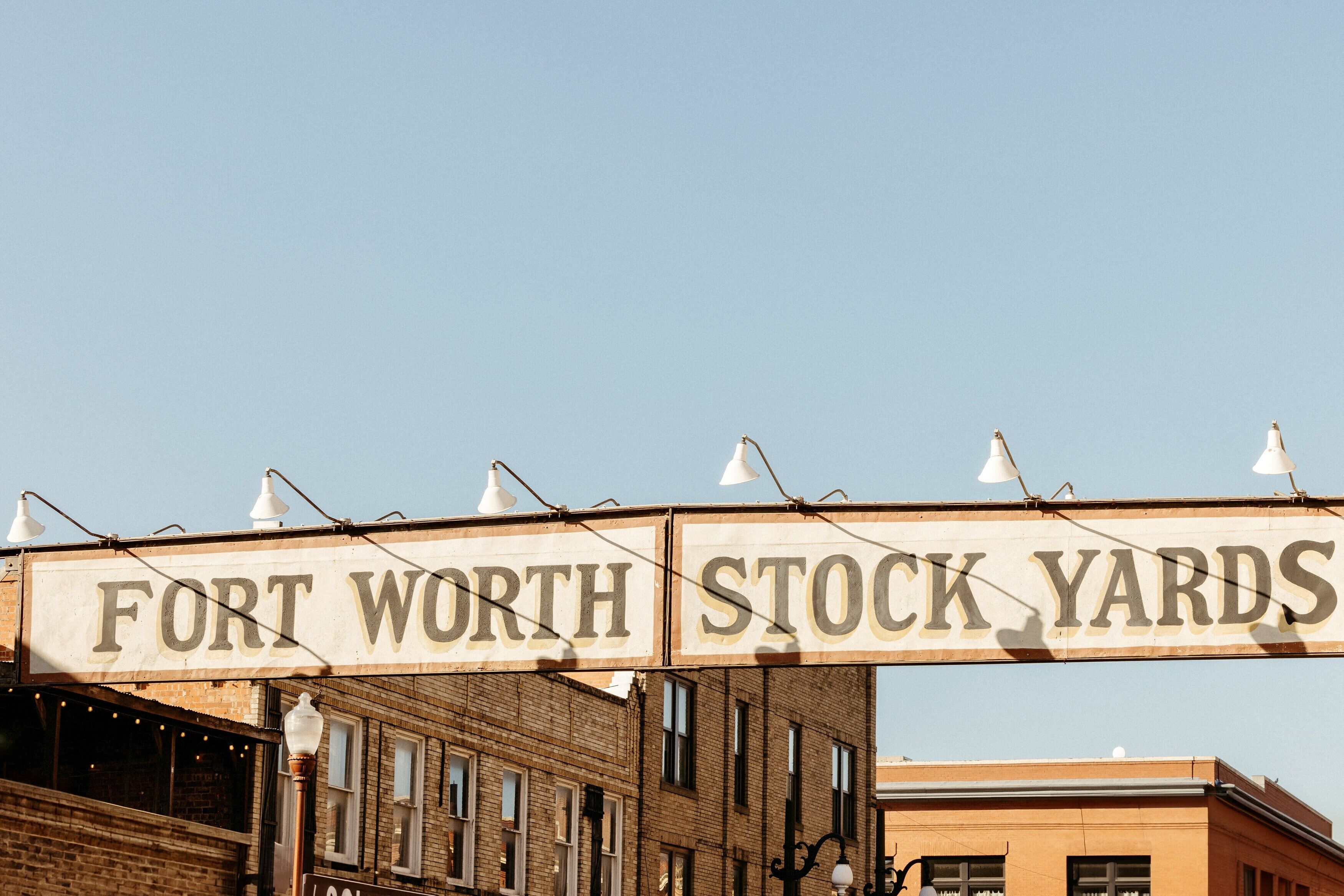 A sign reading "FORT WORTH STOCK YARDS" above a building with brick walls and multiple windows.