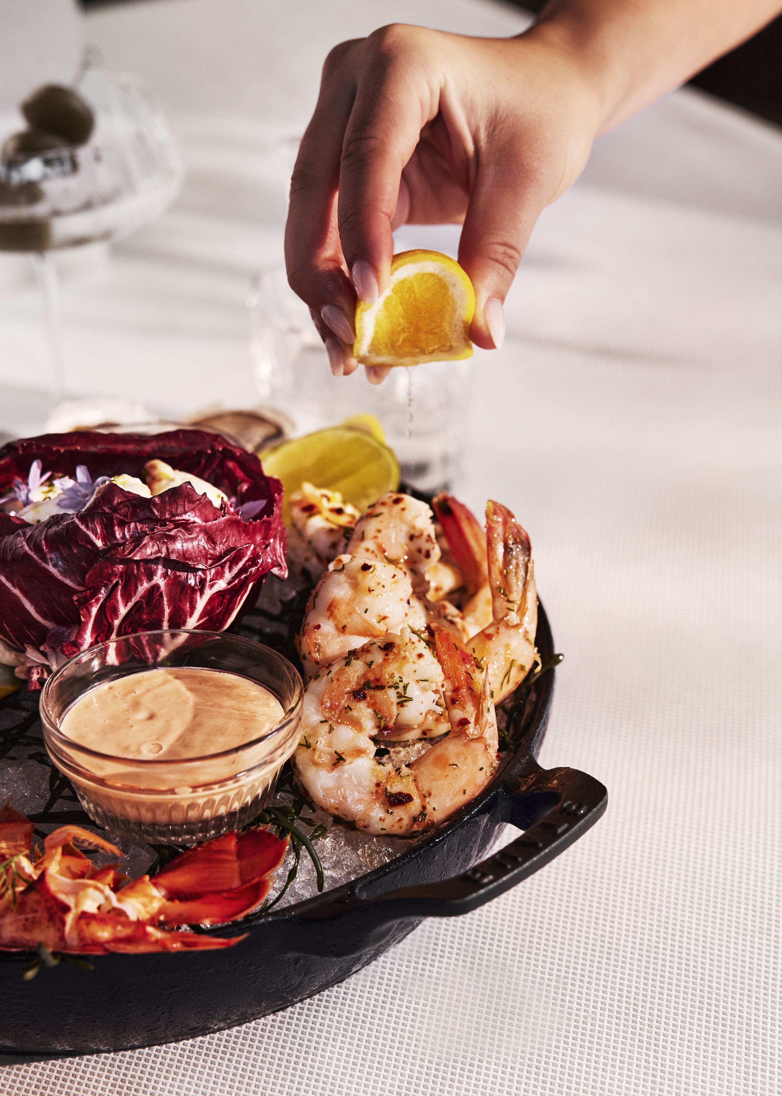 A seafood dish with shrimp, red cabbage, and lemon on a black plate, accompanied by a bowl of sauce.