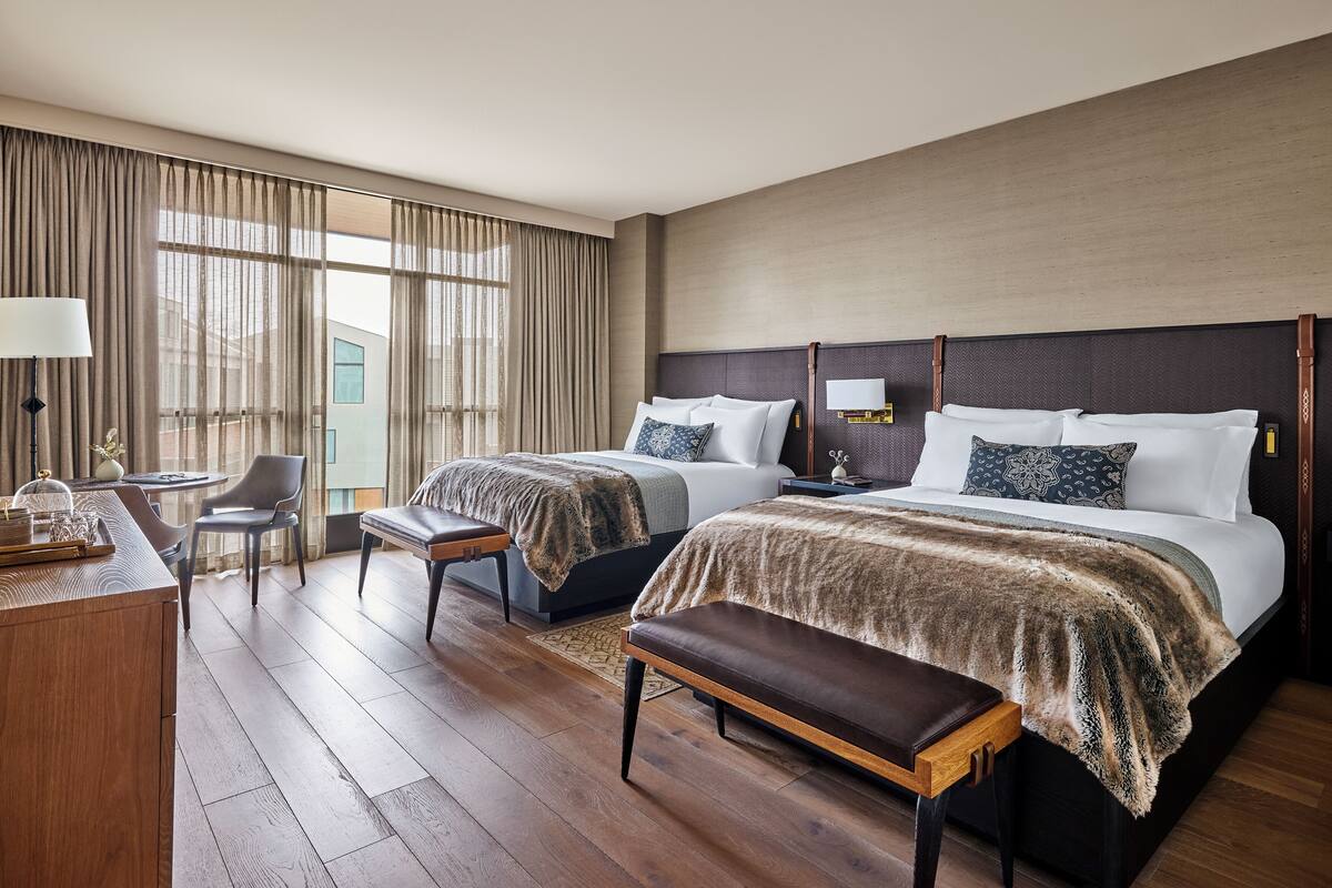 A hotel room with two beds, a desk, a chair, and a bench.