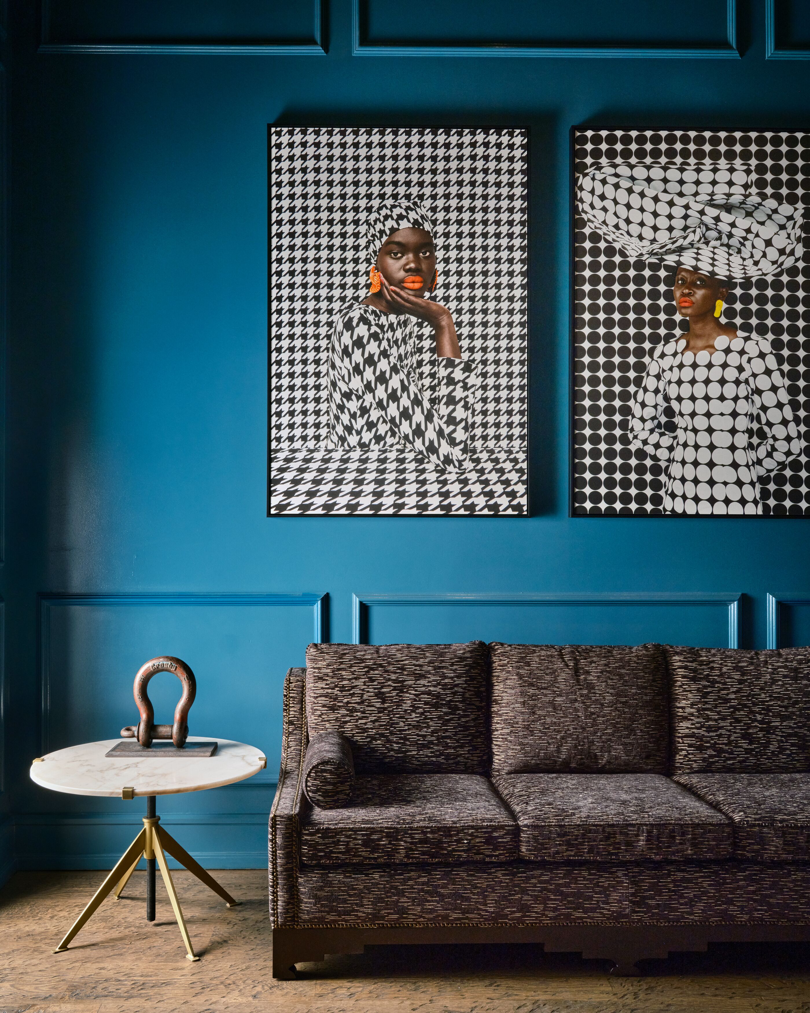 A room with a blue wall, a patterned sofa, and two framed artworks.