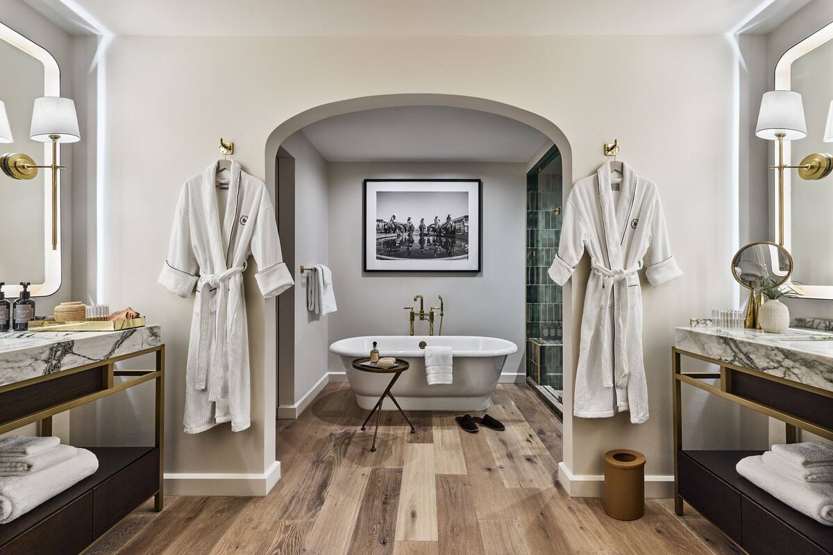 A modern bathroom with a freestanding bathtub, two vanity mirrors, and a framed black-and-white photograph on the wall.