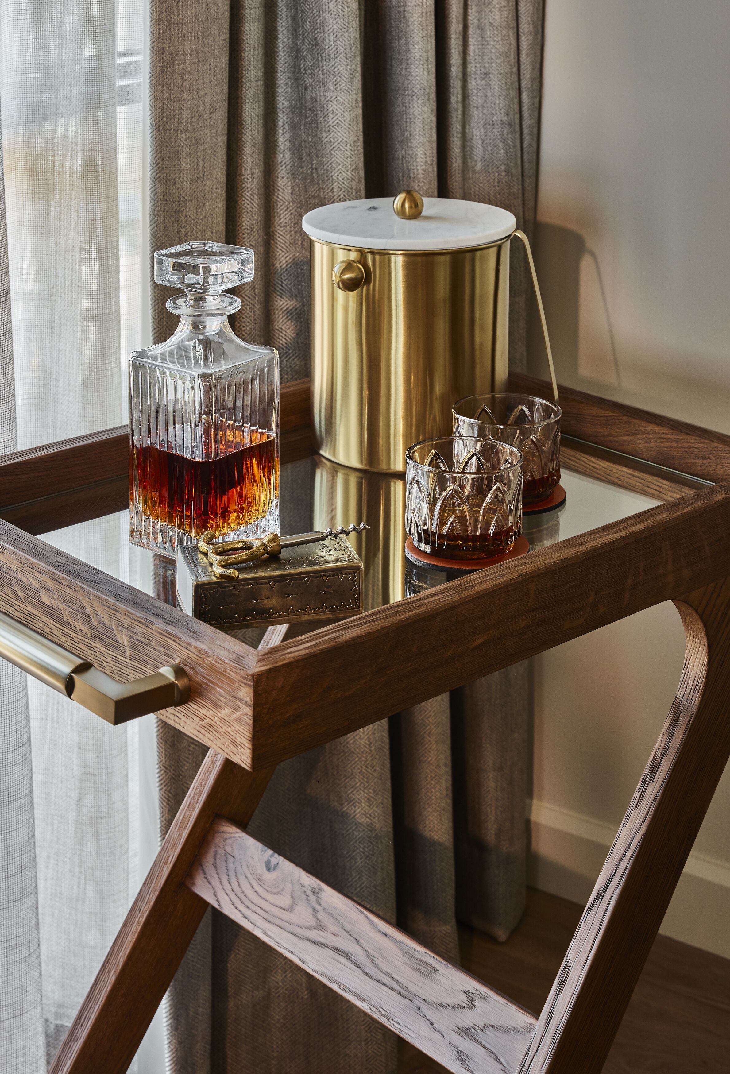 Una mesa de vidrio con una botella y vasos, una olla dorada y una silla de madera.