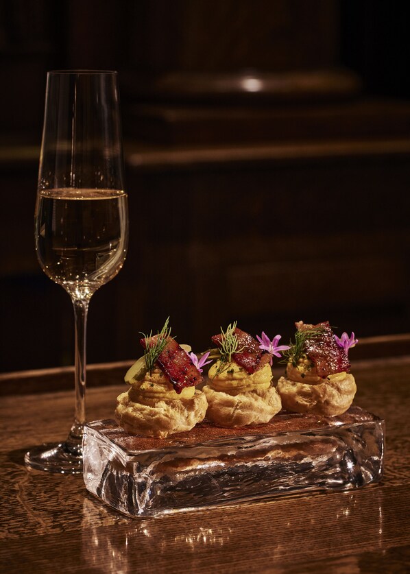 Una copa de vino blanco y tres aperitivos gourmet sobre un plato de vidrio transparente.