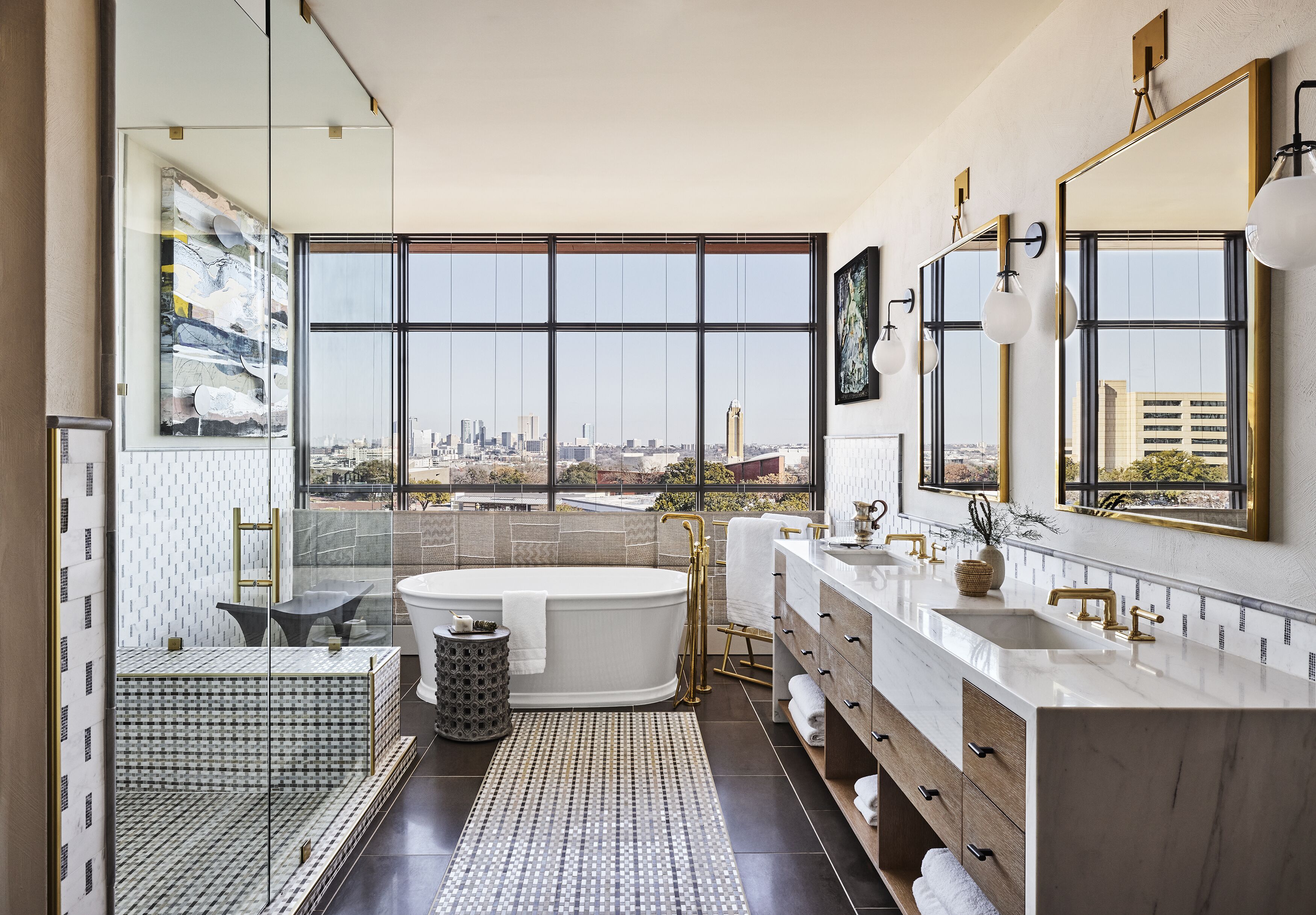 Un baño moderno con una bañera grande, lavamanos dobles y vistas a la ciudad a través de amplias ventanas.