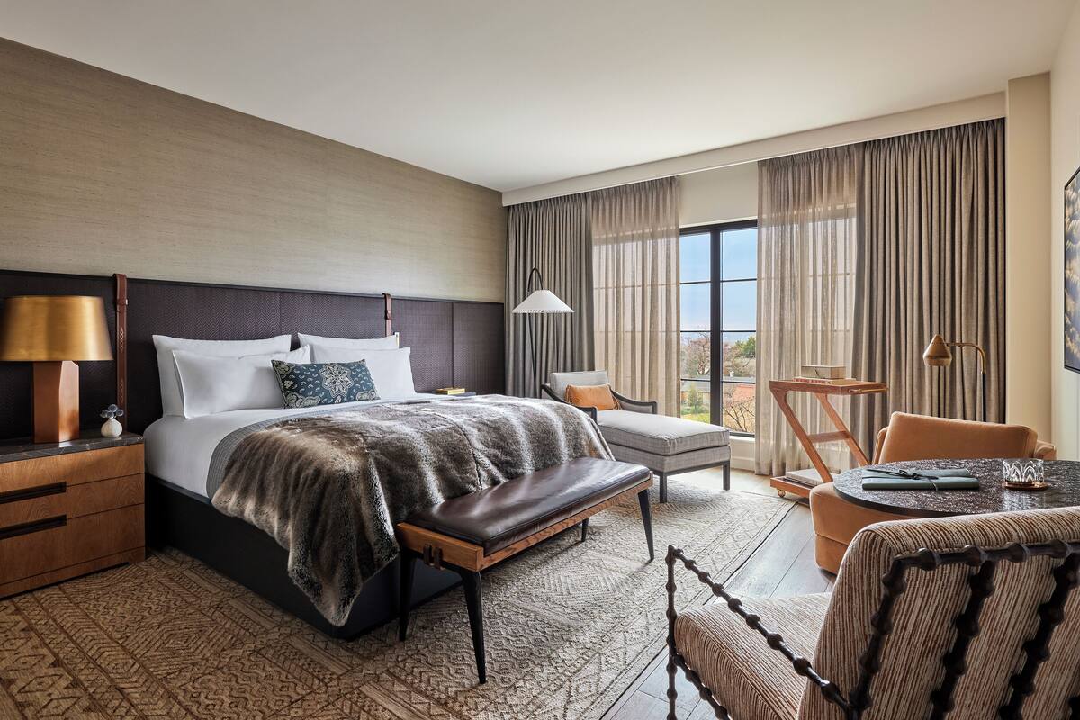 A hotel room with a large bed, a desk, a chair, and a view of the outdoors.