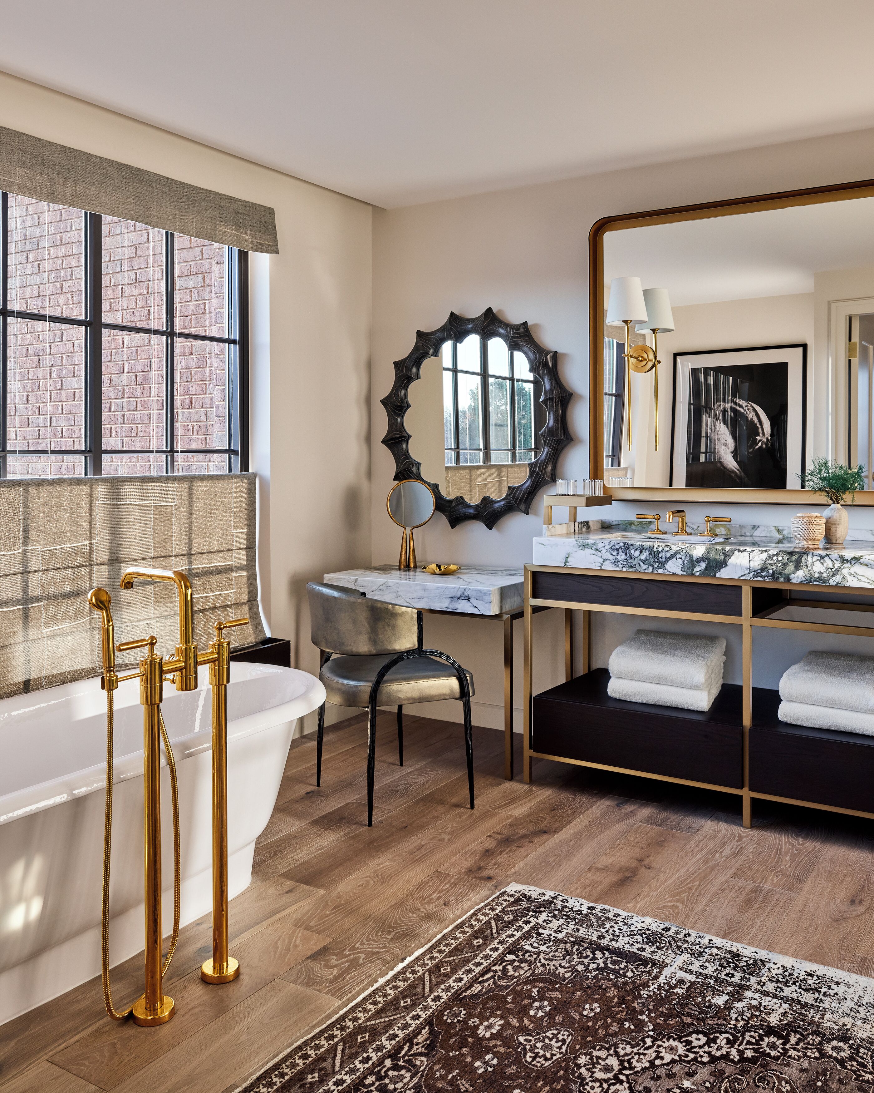 A modern bathroom with a freestanding bathtub, a vanity with a marble countertop, a large mirror, and a patterned rug on the floor.