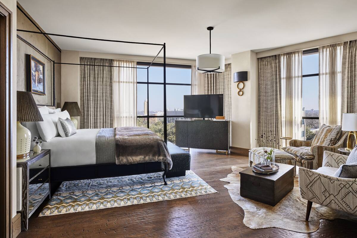 A modern hotel room with a large bed, a TV, a sofa, and a view of the city.