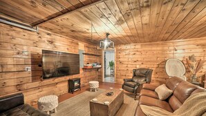 Ein gemütliches Blockhaus-Interieur mit Holzwänden, einem Ledersofa, einem Fernseher und einem Kamin.