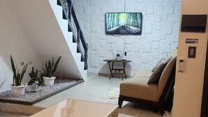 Un salon moderne avec un plancher en bois, un canapé, une table à manger avec une assiette, un téléviseur fixé à un mur blanc et un escalier.