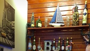 Un espace bar avec des étagères en bois où sont exposées différentes bouteilles d'alcool, un panneau néon et une pancarte de bienvenue.