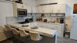A modern kitchen with white cabinetry, a central island with bar stools, a built-in oven, and various appliances.