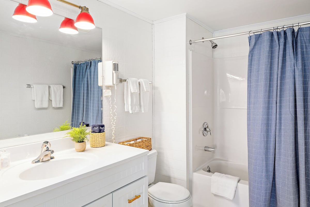 A modern bathroom with a white sink, a mirror, a shower with a blue curtain, and a white toilet.