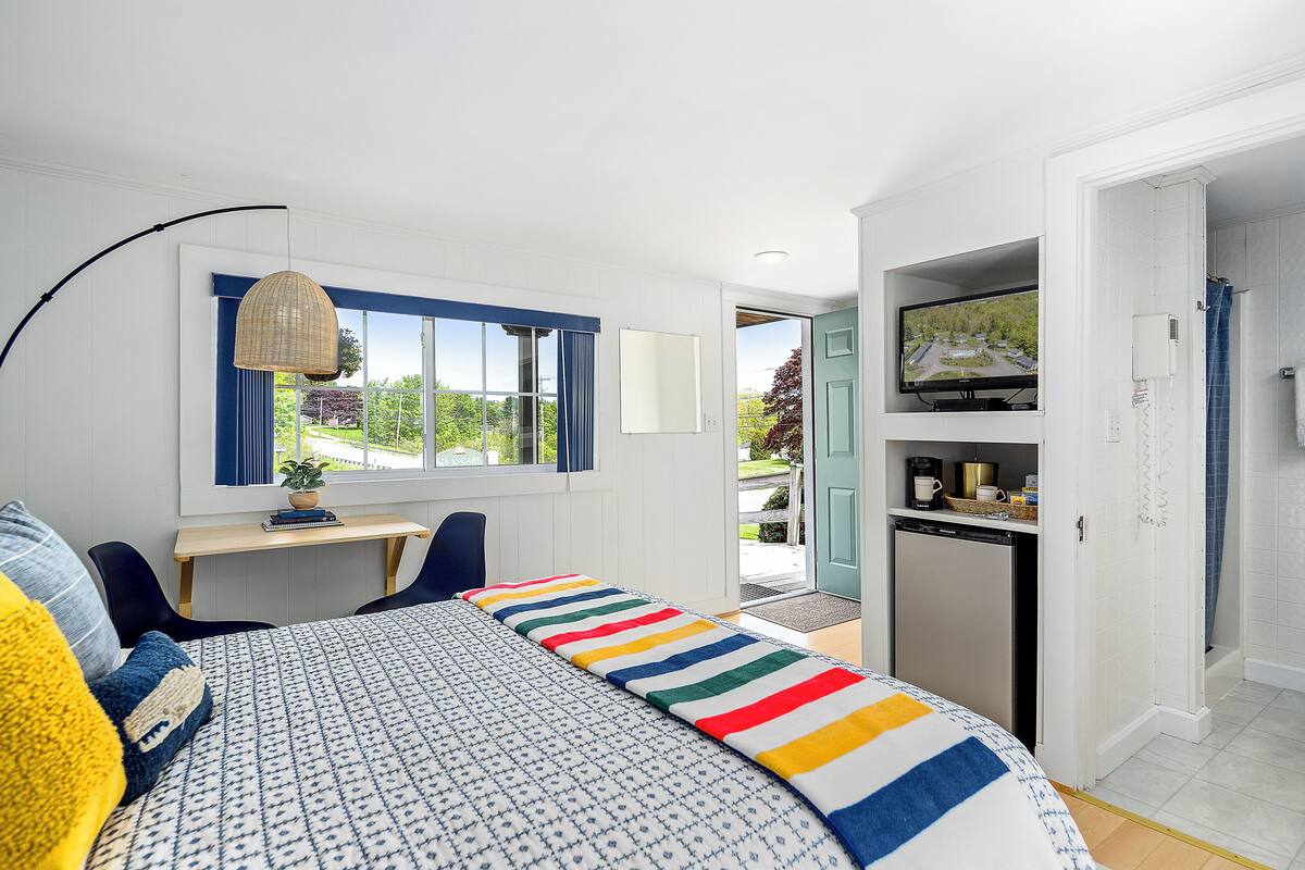 A bedroom with a bed, a desk, a television, and a view of the outdoors.