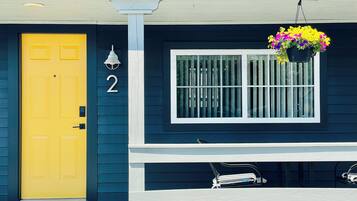 A house with a yellow door, a number '2' on the wall, a window with bars, and a hanging flower pot.