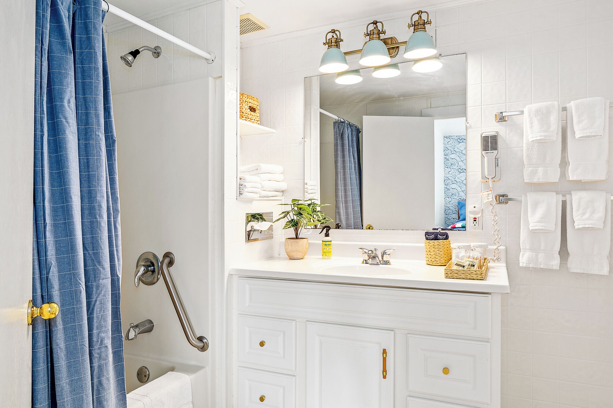 Une salle de bain avec un meuble-lavabo blanc, un miroir, une douche avec un rideau bleu et un porte-serviettes avec plusieurs serviettes.