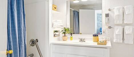 Une salle de bain avec un meuble-lavabo blanc, un miroir, une douche avec un rideau bleu et un porte-serviettes avec plusieurs serviettes.