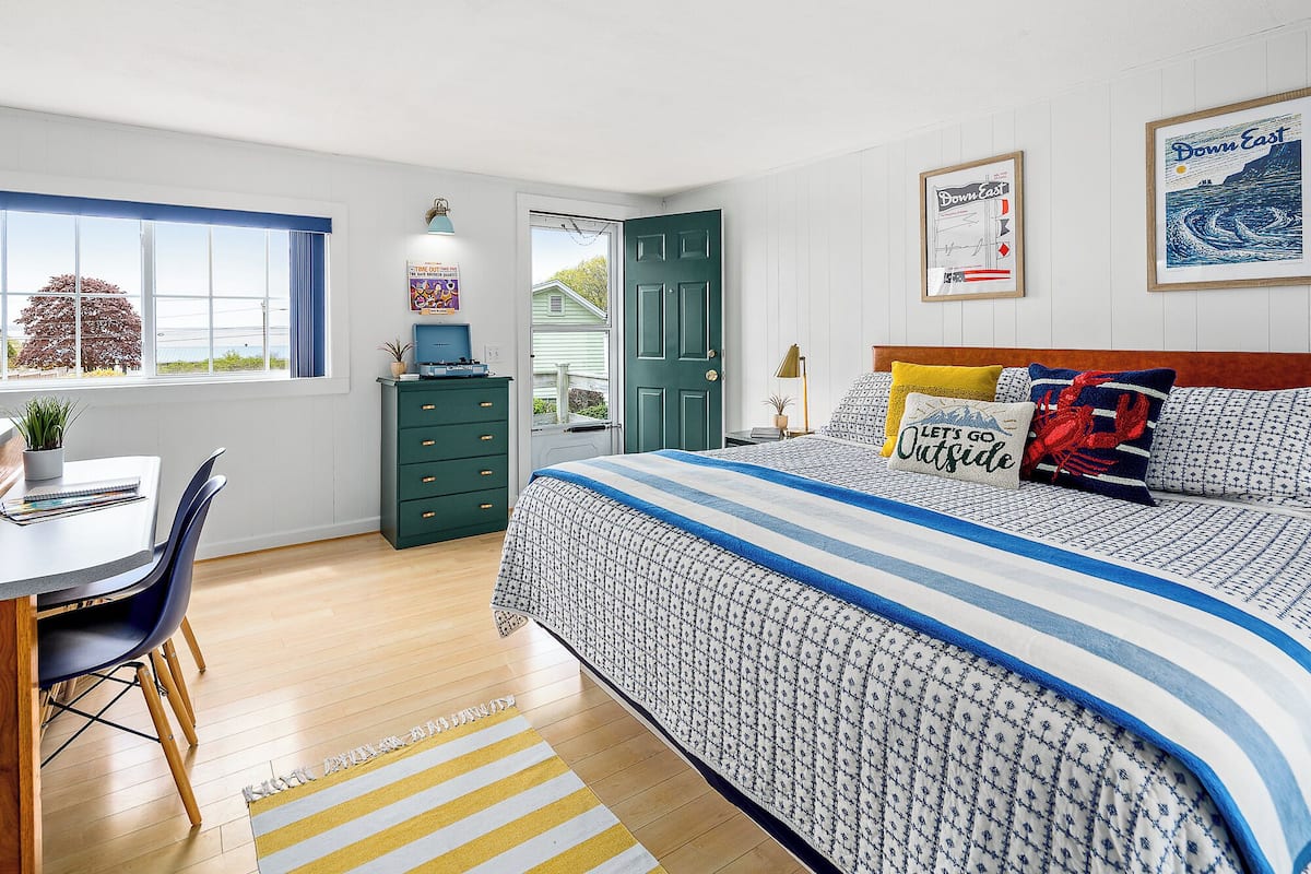 A bedroom with a bed, a desk, a chair, a dresser, and a window.
