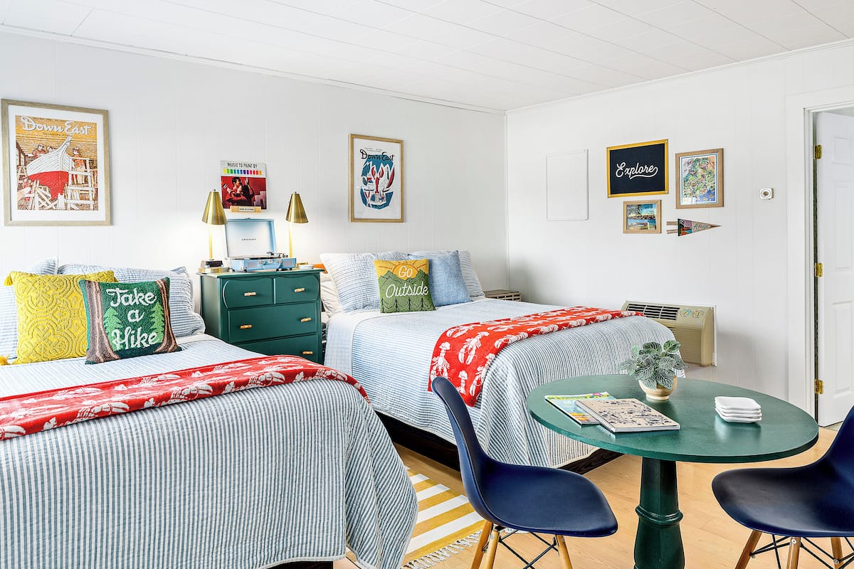 A well-lit, modern room with two beds, a green table with chairs, and various wall art.